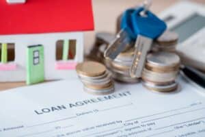 A loan agreement form, house model, keys, coins, and calculator arranged on a table—perfect for discussing FHA Loans for Low Credit Scores.