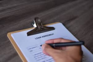 A person signs a loan agreement form on a clipboard with a pen on a wooden surface, securing DSCR Loans for Property Investors.