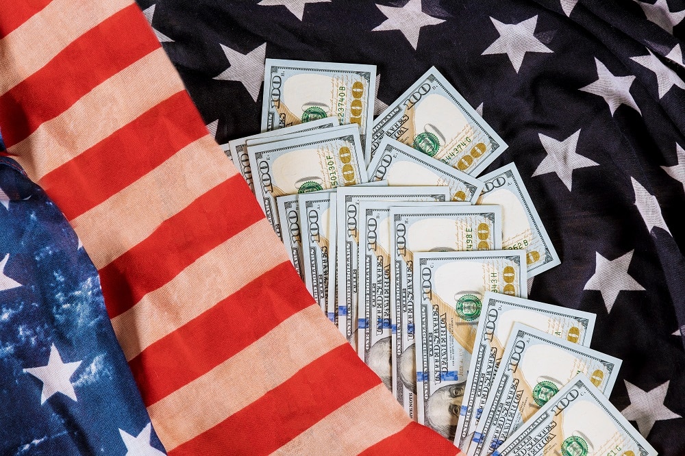 Several US $100 bills are arranged in a fan shape on top of an American flag featuring stars and stripes, symbolizing financial freedom and showing how VA Loans work to support American veterans.