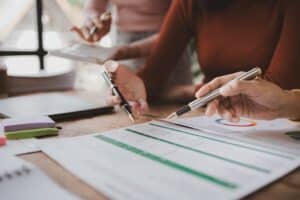 Two people review documents and charts at a desk, pens in hand, discussing data on Hard Money vs Traditional Loans and financial reports with colorful sticky notes nearby.
