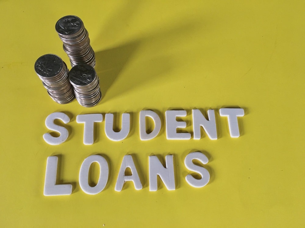 Stacks of coins and the words "STUDENT LOANS" spelled out in white letters on a yellow background highlight the impact of student loans on mortgage approval.